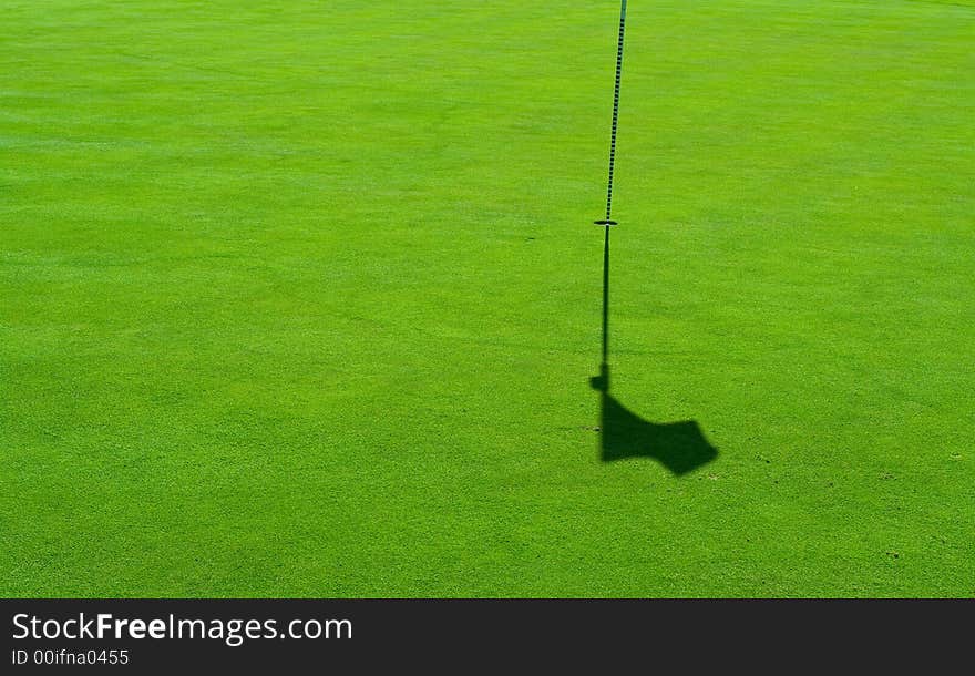 A hole with a flag pole and a shadow on a perfect green grass. A hole with a flag pole and a shadow on a perfect green grass