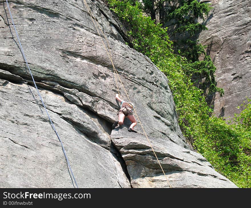 Young woman begins her climb on steep rock face. Young woman begins her climb on steep rock face.