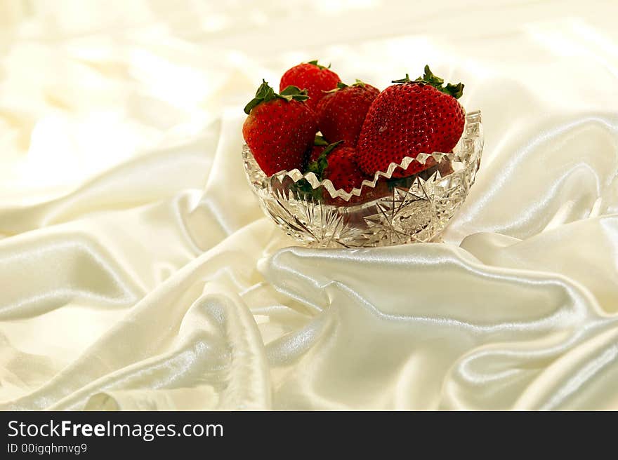 Scrumptuous red strawberries in a crystal bowl against a white satin background. Scrumptuous red strawberries in a crystal bowl against a white satin background