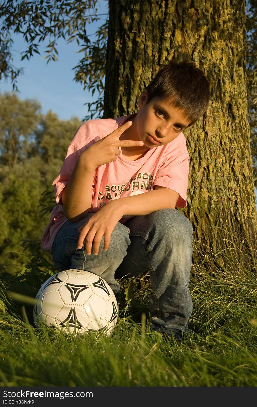 Boy shows the peacesign and holds a soccerball. Boy shows the peacesign and holds a soccerball