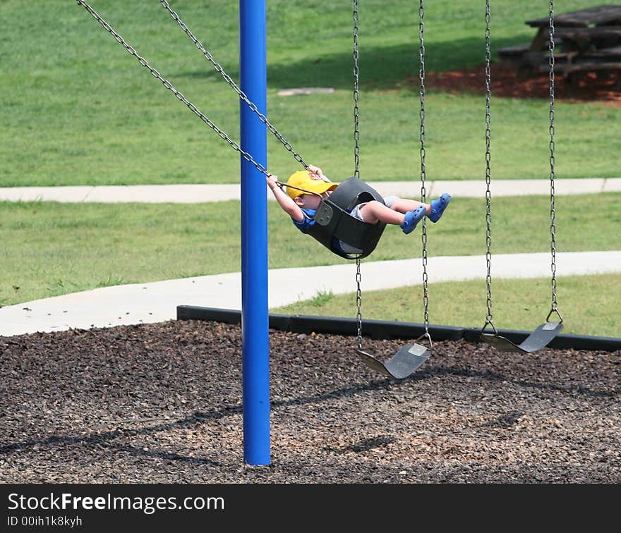 A small child wearing a cap on a park swing. A small child wearing a cap on a park swing