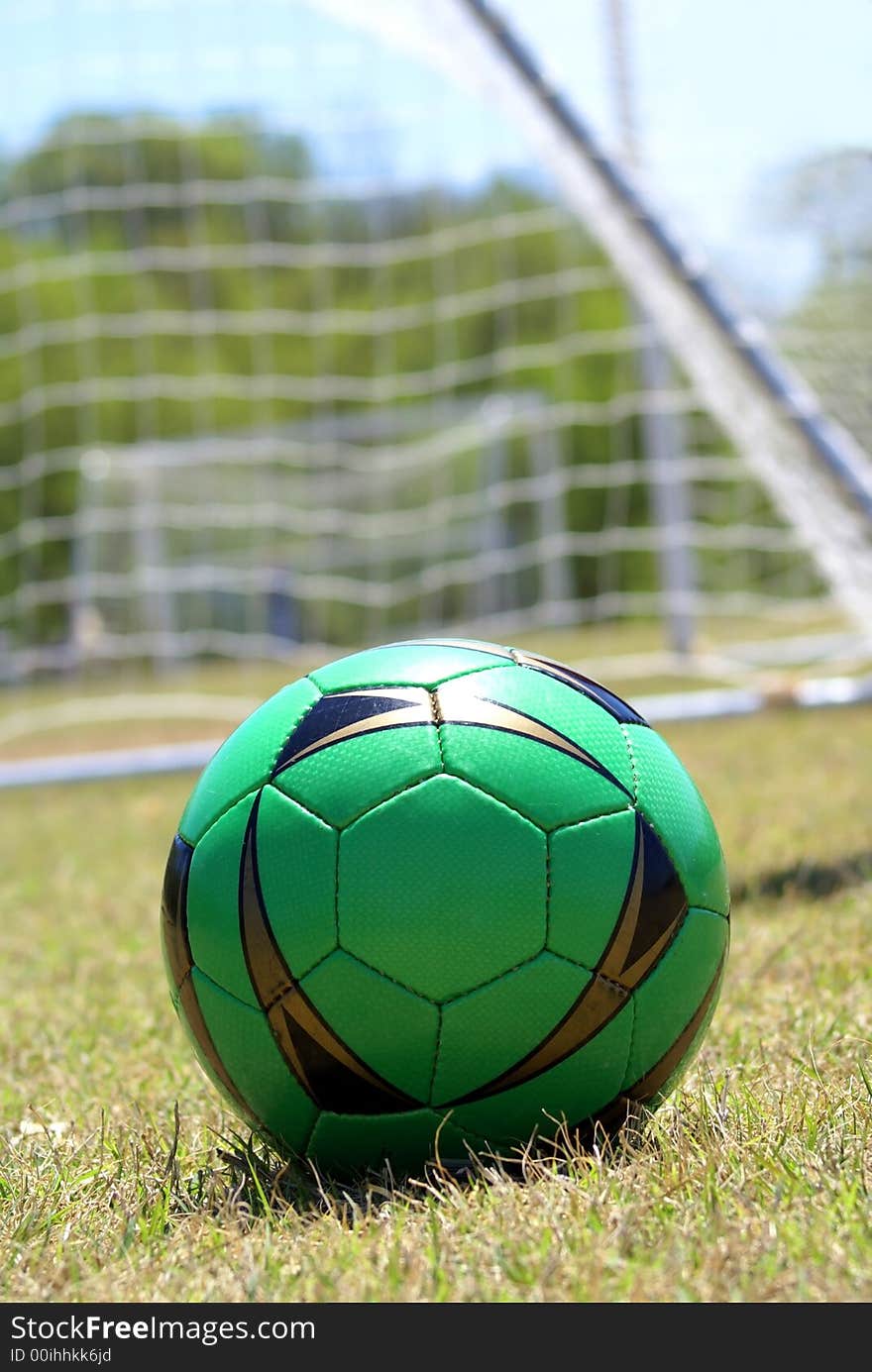 Green soccer ball with net in the background on dried out soccer field. Green soccer ball with net in the background on dried out soccer field