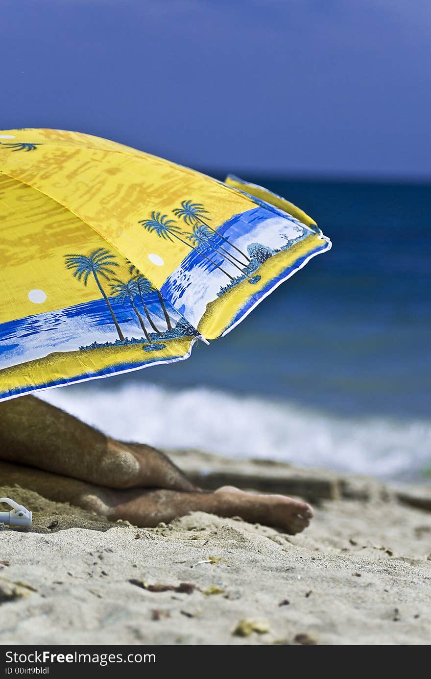 Man resting under a big colorful umbrella on a sunny beach