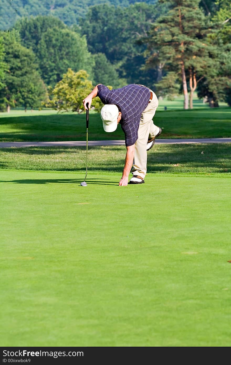 A male golfer bends to retrieve his ball from the hole. Space for copy in foreground. A male golfer bends to retrieve his ball from the hole. Space for copy in foreground.