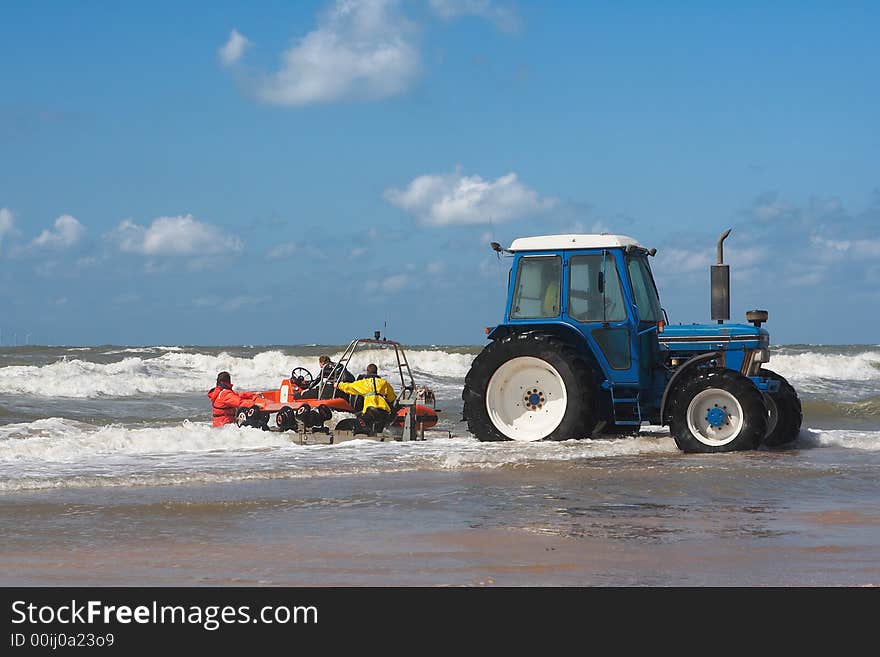 Action shot of a blue tractor in sea water launching a sea rescue raft with 3 people. Hi waves, blue sky with some clouds. Action shot of a blue tractor in sea water launching a sea rescue raft with 3 people. Hi waves, blue sky with some clouds