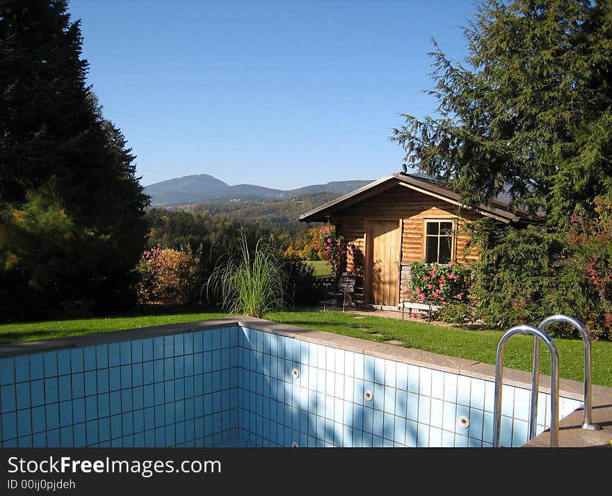 Spring landscape of a garden with an empty swimming pool and a wooden cottage