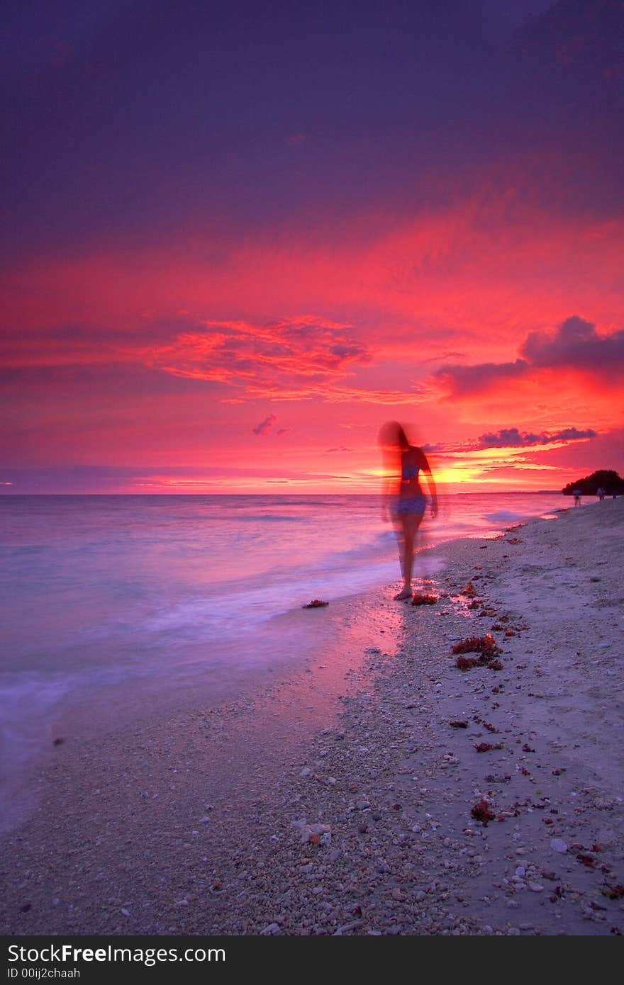 An attractive single woman walking on a beautiful tropical paradise beach at sunset beside a calm sea while on a relaxing vacation. An attractive single woman walking on a beautiful tropical paradise beach at sunset beside a calm sea while on a relaxing vacation