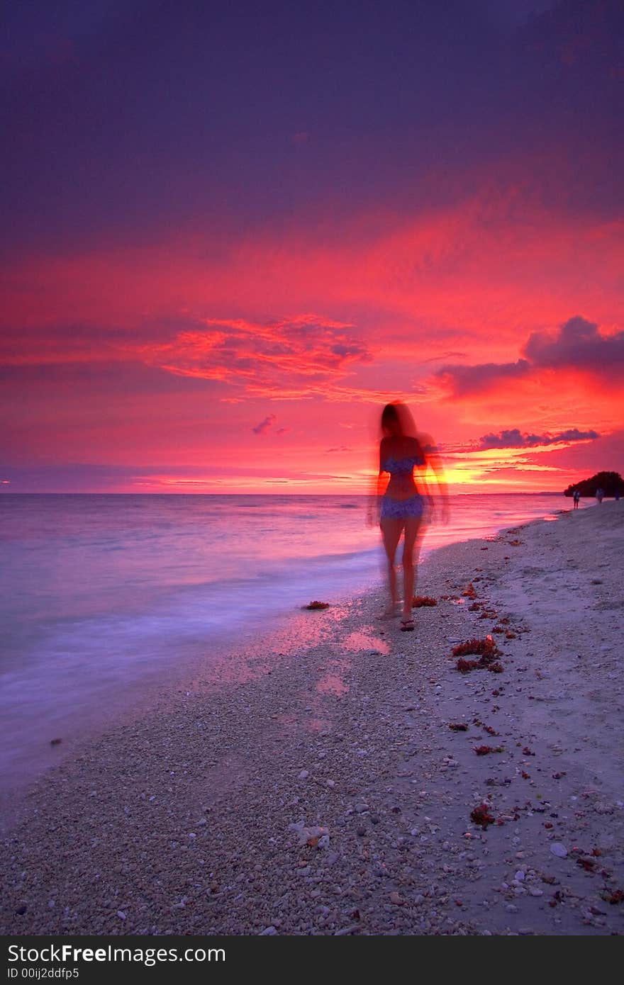 An attractive single woman walking on a beautiful tropical paradise beach at sunset beside a calm sea while on a relaxing vacation. An attractive single woman walking on a beautiful tropical paradise beach at sunset beside a calm sea while on a relaxing vacation