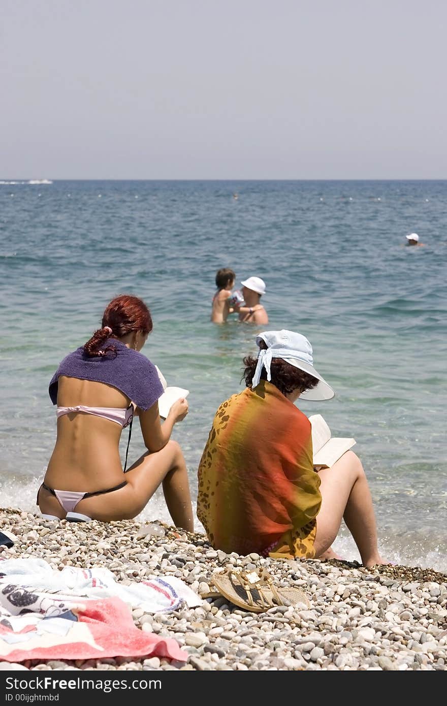 Beautiful young girl and her mother relaxing by the seasideand reading a book