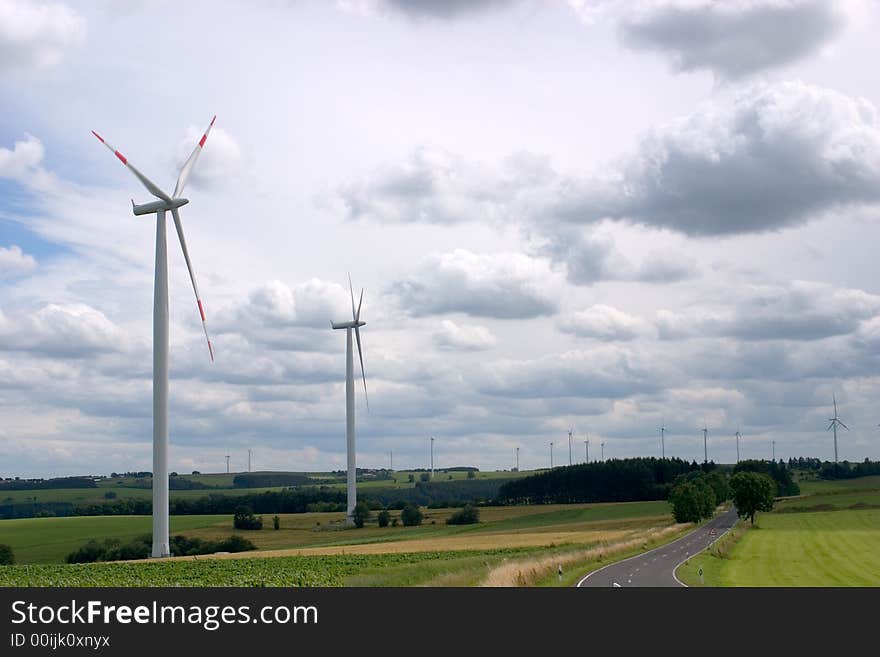 Two wind turbines, with more in the rear, against a sky of dramatic clouds