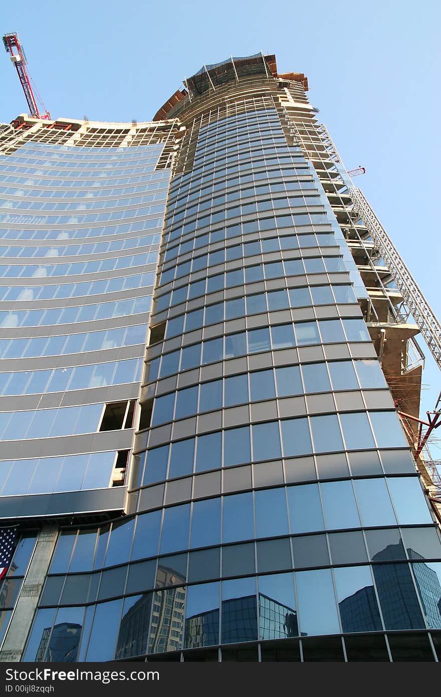 A modern glass skyscraper under construction with a reflection. A modern glass skyscraper under construction with a reflection