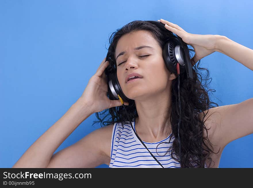 young beautiful girl listening music on blue background