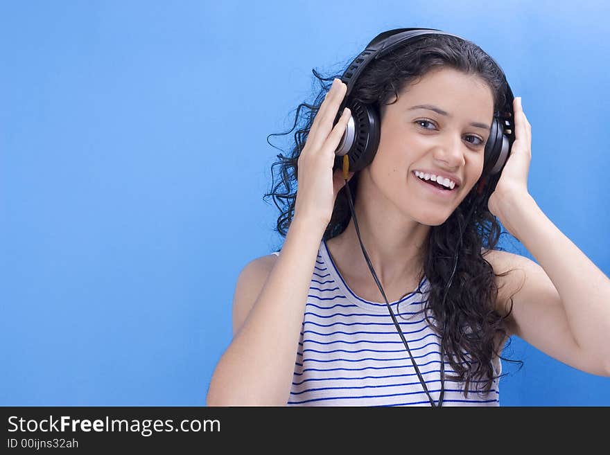 Young beautiful girl listening music on blue background