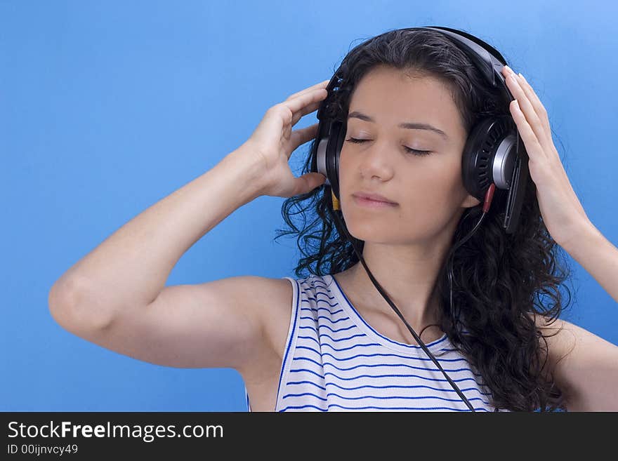 Young beautiful girl listening music on blue background