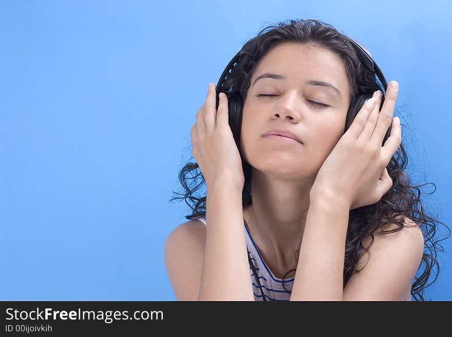 Young beautiful girl listening music on blue background