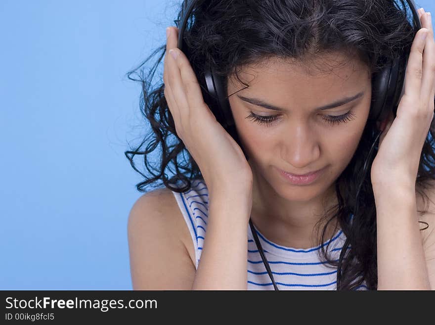 Young beautiful girl listening music on blue background