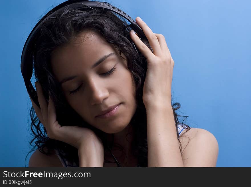 Young beautiful girl listening music on blue background