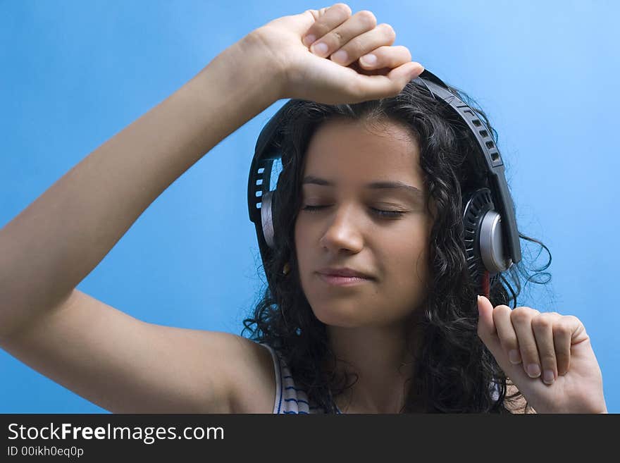 Young beautiful girl listening music on blue background