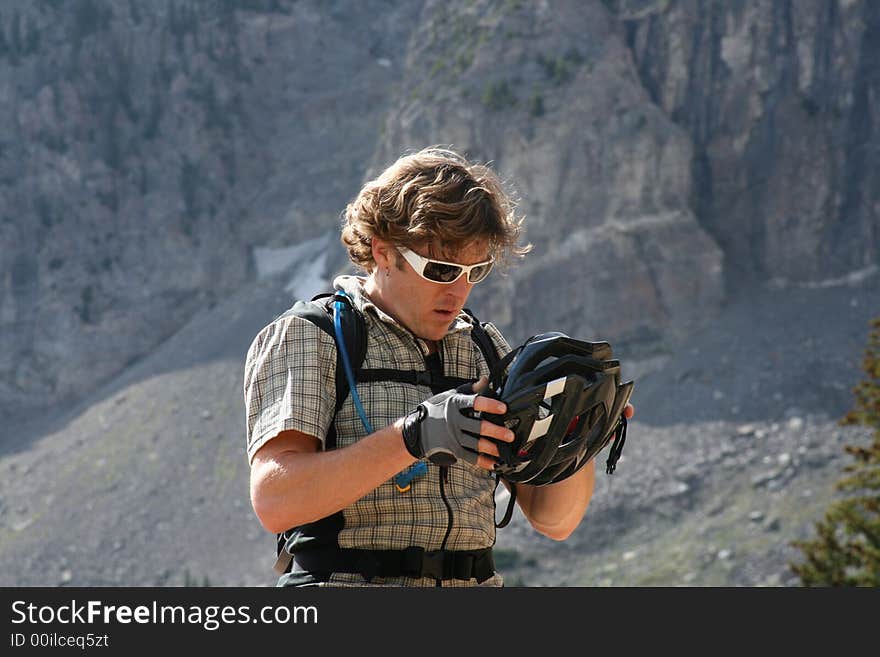 A mountain biker in the mountains checks his helmet. A mountain biker in the mountains checks his helmet