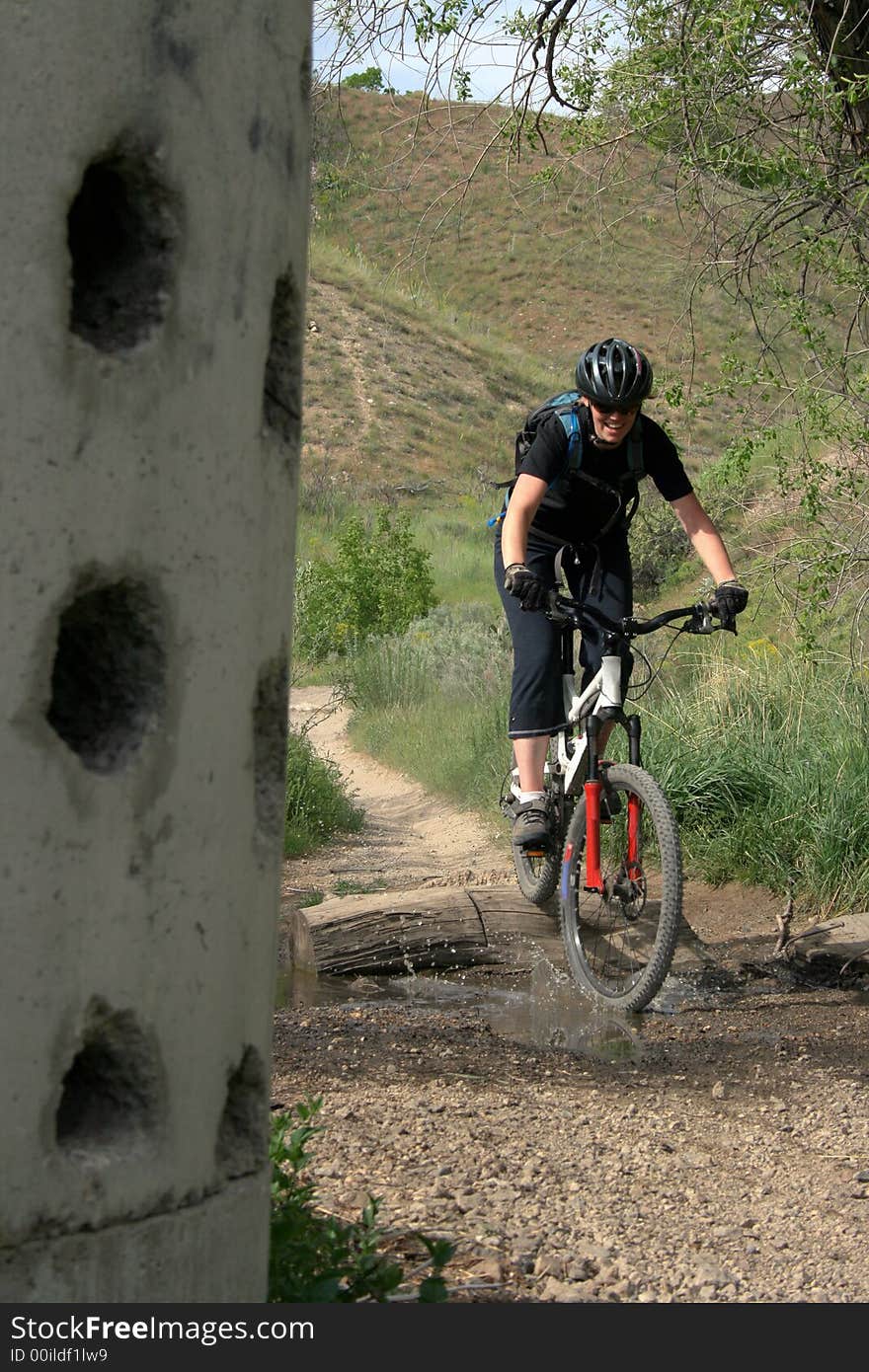 A woman mountain biker in the hills spashes through a puddle. A woman mountain biker in the hills spashes through a puddle