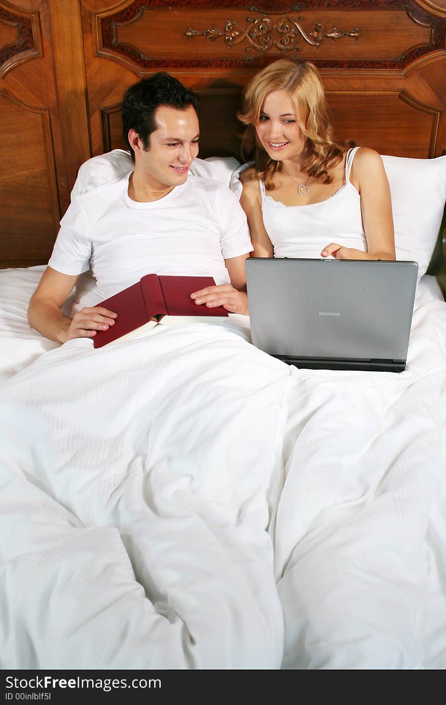 A young woman is showing her boyfriend something interesting on her notebook, while the man is holding a book in his hands. A young woman is showing her boyfriend something interesting on her notebook, while the man is holding a book in his hands