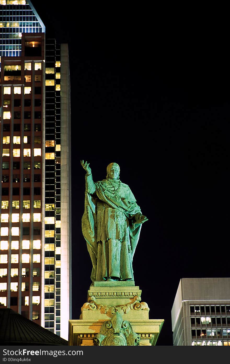 Monseigneur Bourget statue on the backdrop of skyscrapers in Montreal at night.