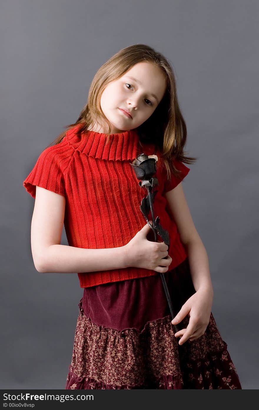 The girl of ten years with an iron rose in hands on a grey background. The girl of ten years with an iron rose in hands on a grey background