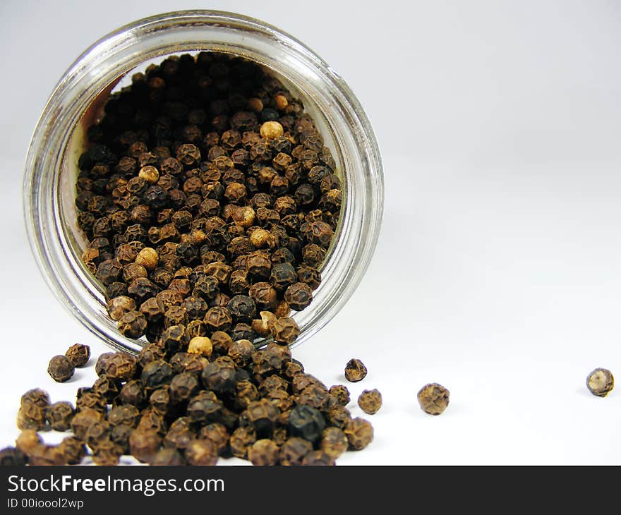 Whole black pepper in a bottle, isolated on white.