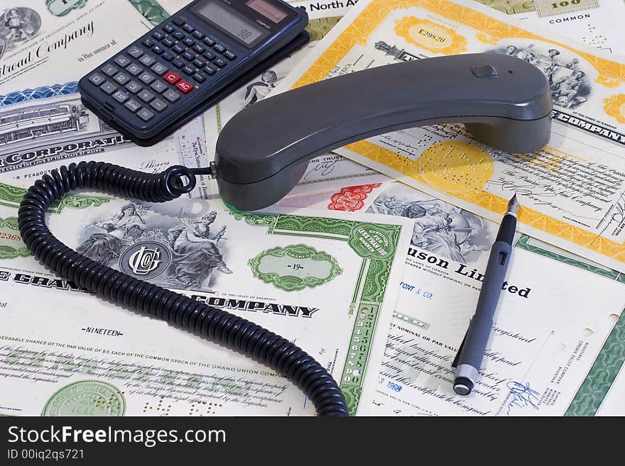 A trader board handset, calculator, and a pen on share certificates. A trader board handset, calculator, and a pen on share certificates