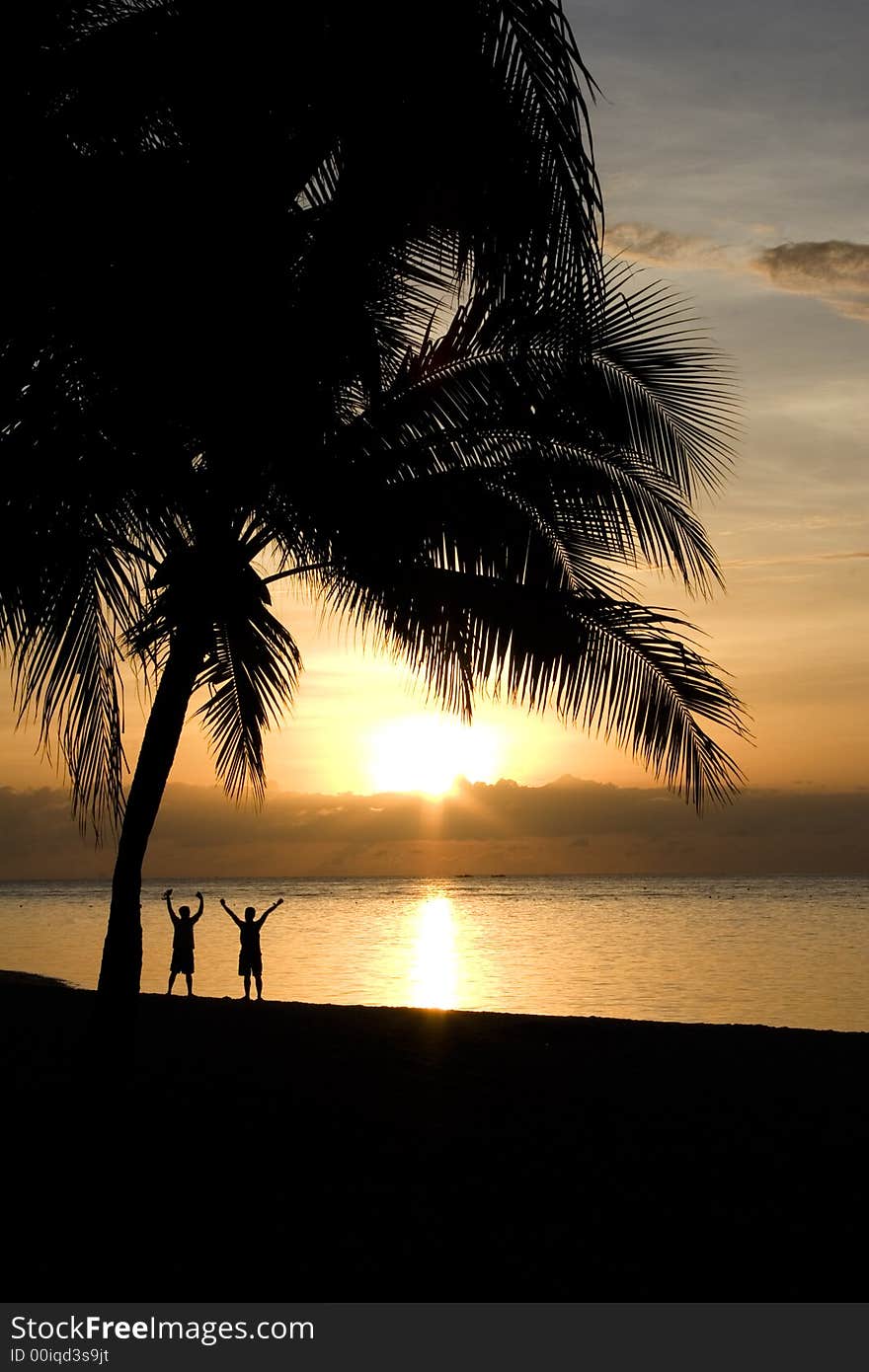 Two people raising their arms at the beach, facing the rising sun. Two people raising their arms at the beach, facing the rising sun.