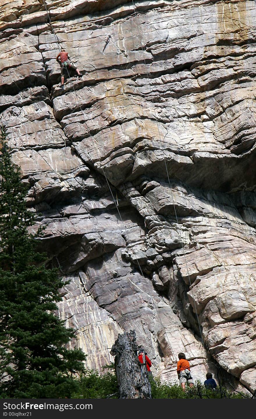 A woman climbs the steep mountain as three friends work the belay lines below. A woman climbs the steep mountain as three friends work the belay lines below