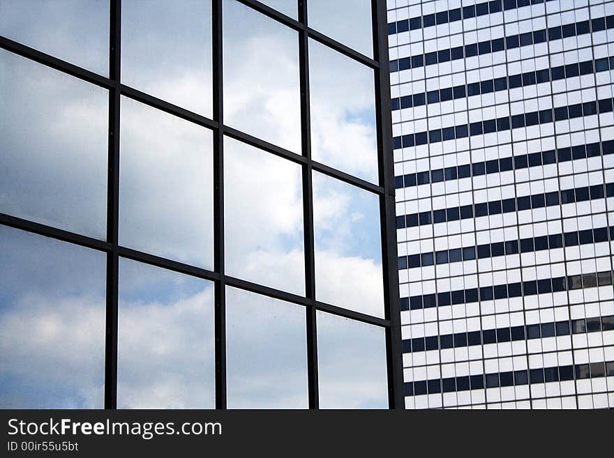 Two buildings in contrast with clouds in the mirror of one building