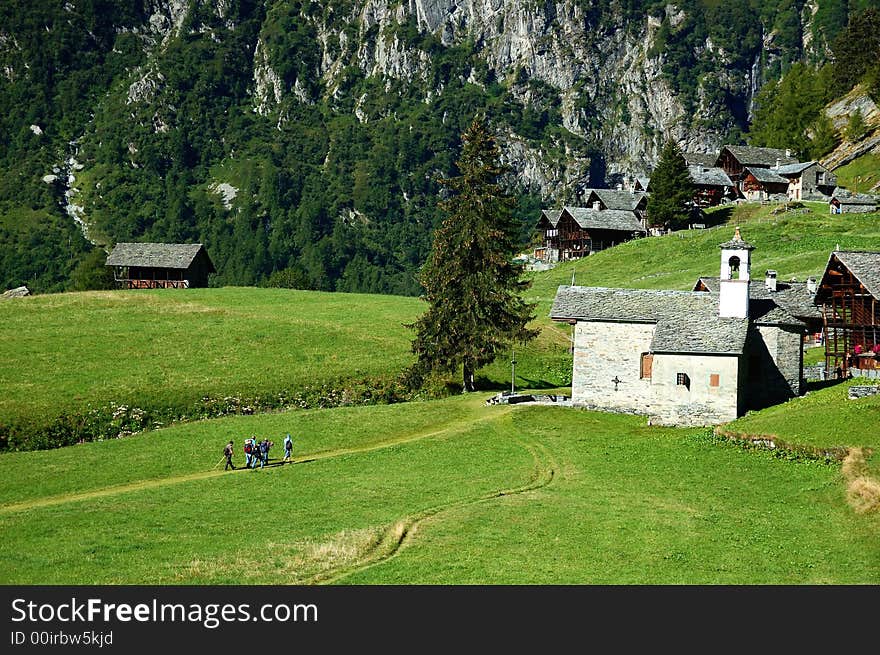 Trekkers walking along a path near a mountain village, west Alps, Italy.