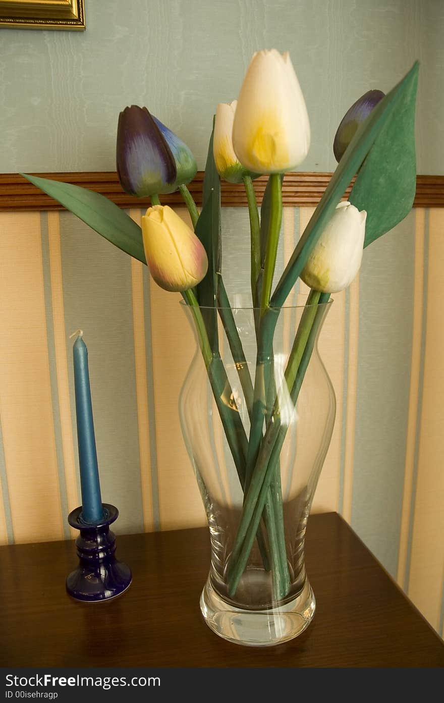 Fresh tulips in the vase on the table with the candle.