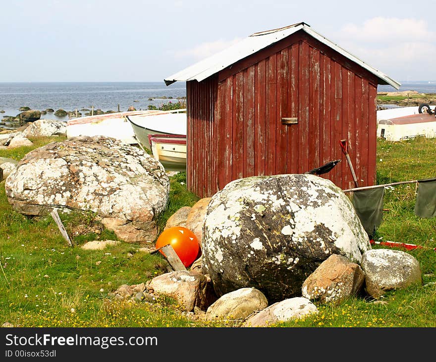 Small red boathouse with some rocks and boats around it.