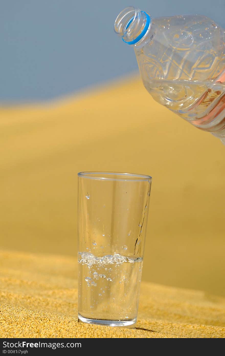 A glass of fresh water and bottle in a desert. Note that the water and bubbles are in motion blur. A glass of fresh water and bottle in a desert. Note that the water and bubbles are in motion blur.
