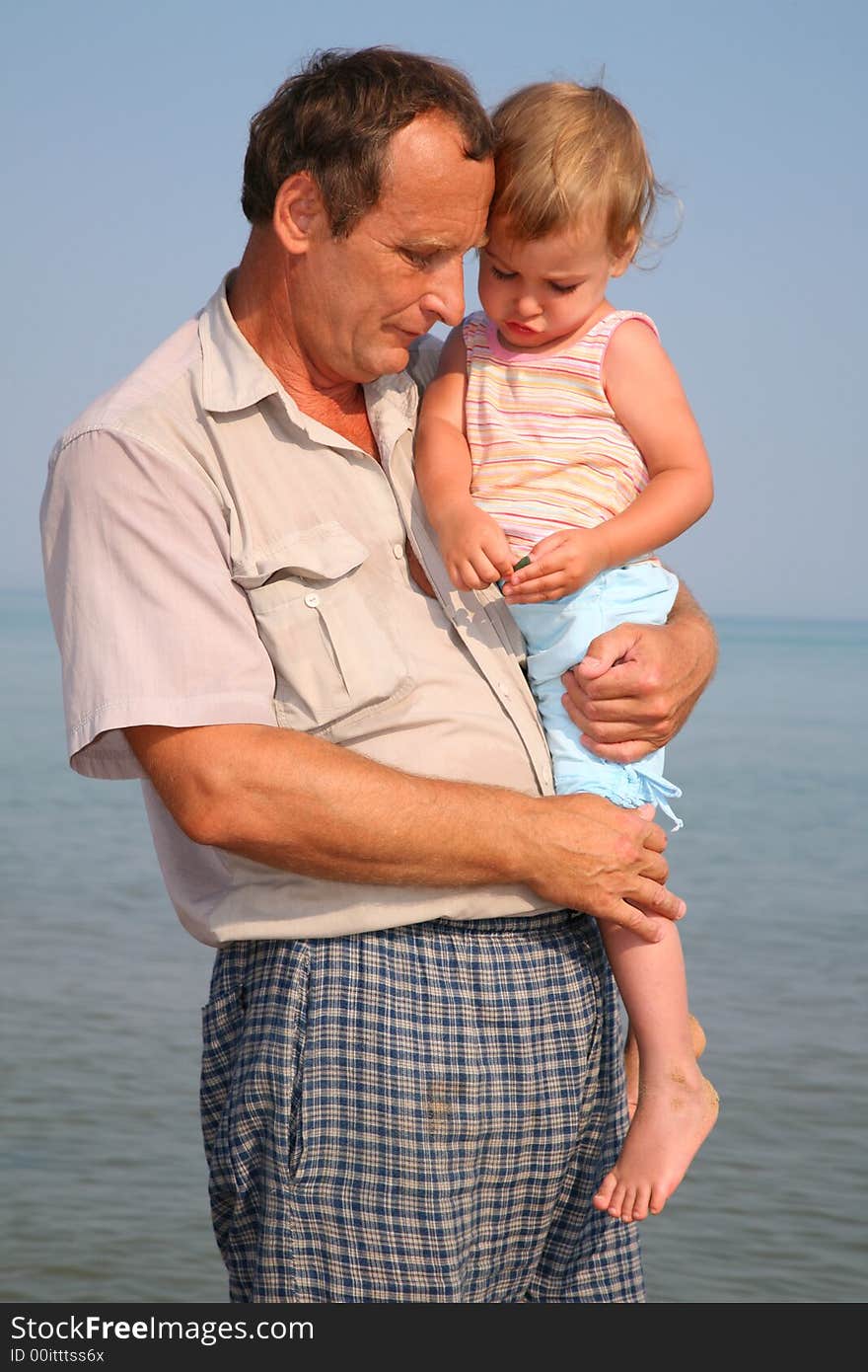 Grandfather holds granddaughter on hands at sea. Grandfather holds granddaughter on hands at sea