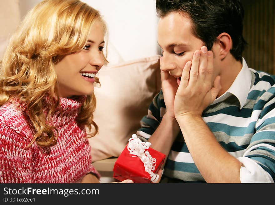 A young attractive couple in christmas time - she is holding a gift in front of a chimney. A young attractive couple in christmas time - she is holding a gift in front of a chimney