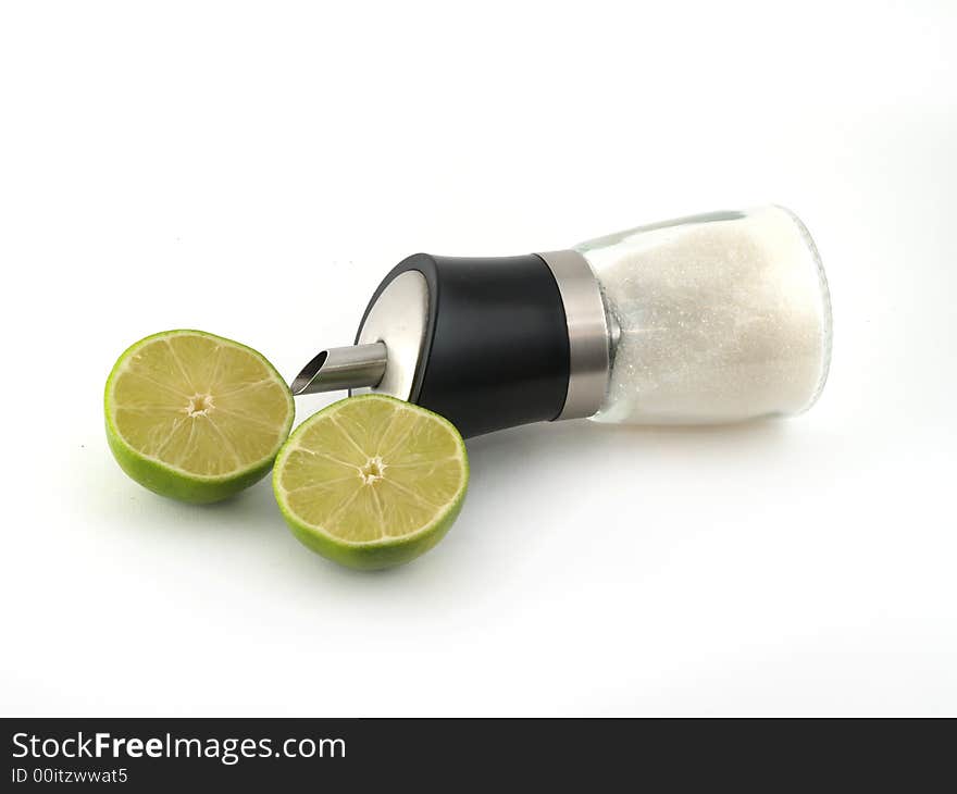 Two halves of green lime and sugar dispenser liyng on the white background