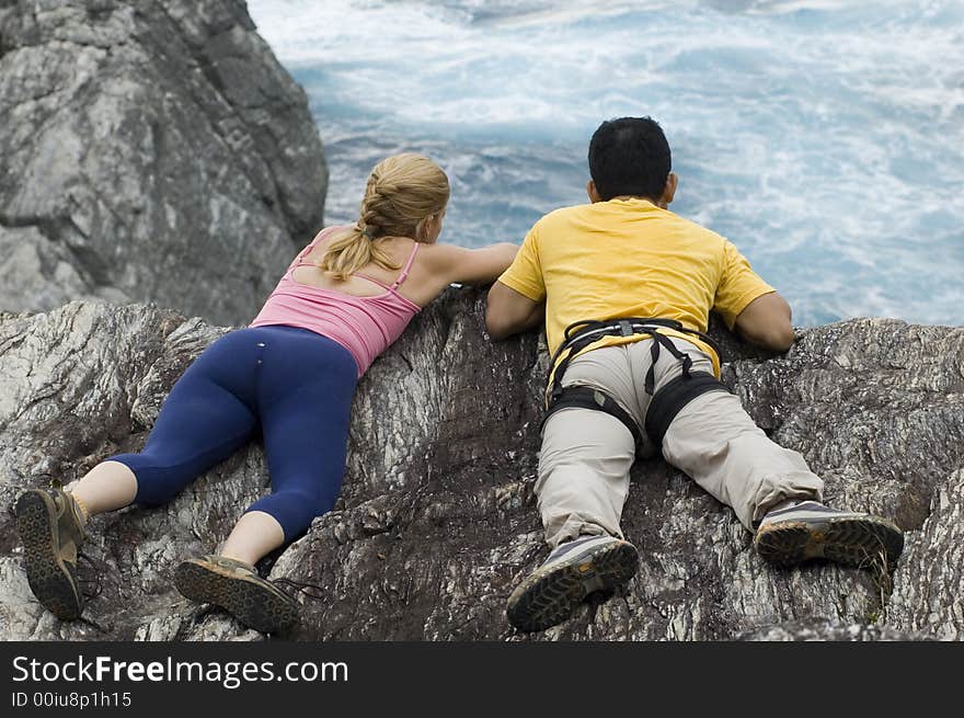 Two rock climbers looking at ocean below a sea cliff