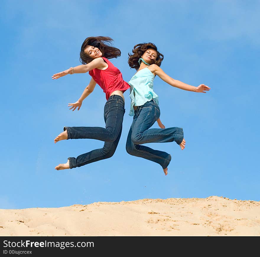 Two girlfriends jump with happiness on sand. Two girlfriends jump with happiness on sand