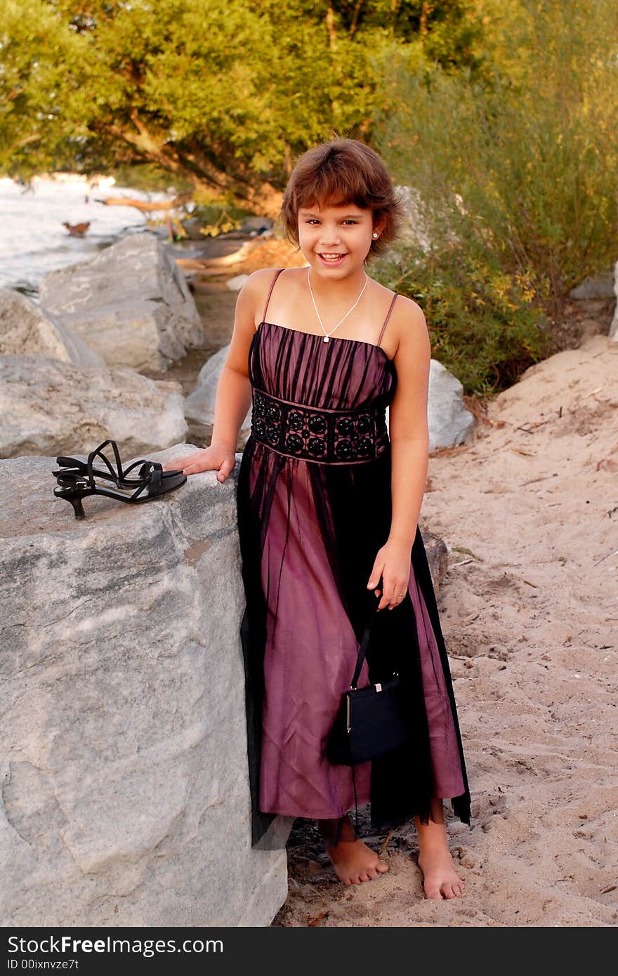 Full-body portrait of an elementary girl in formalwear barefoot on the beach. Full-body portrait of an elementary girl in formalwear barefoot on the beach.