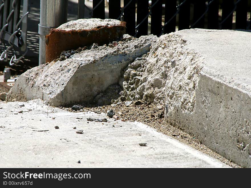 Remains of a rusted pole and broken cement against a chain link fence. Remains of a rusted pole and broken cement against a chain link fence