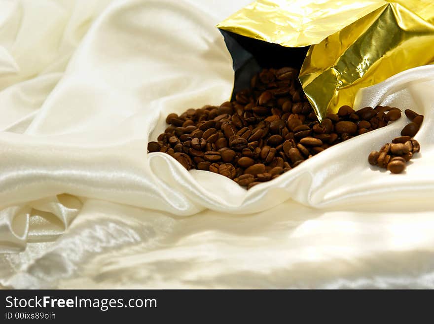 Fresh roasted coffee beans pouring out of bag on satin fabric. Fresh roasted coffee beans pouring out of bag on satin fabric