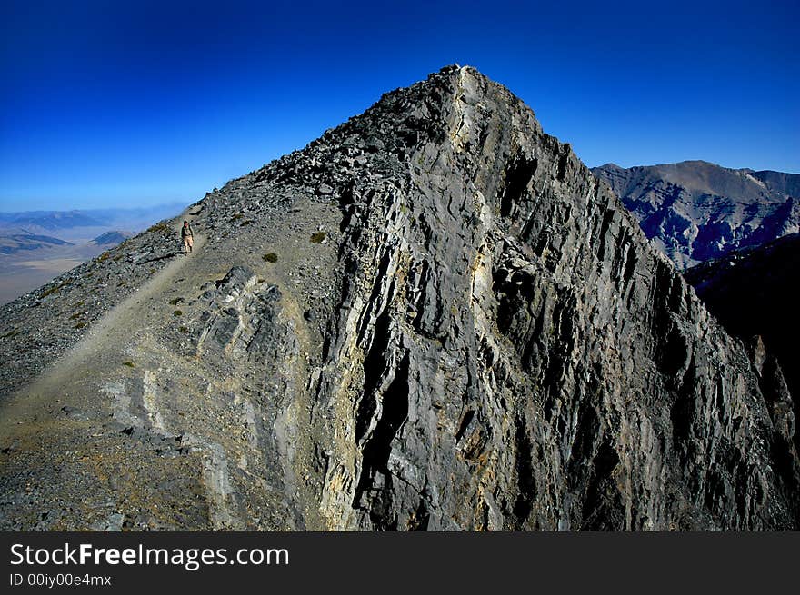 One person walking along trail with mountains in background. One person walking along trail with mountains in background