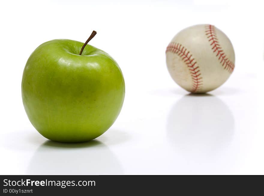 Green granny smith apple and a baseball on white background, symbols of summertime in America