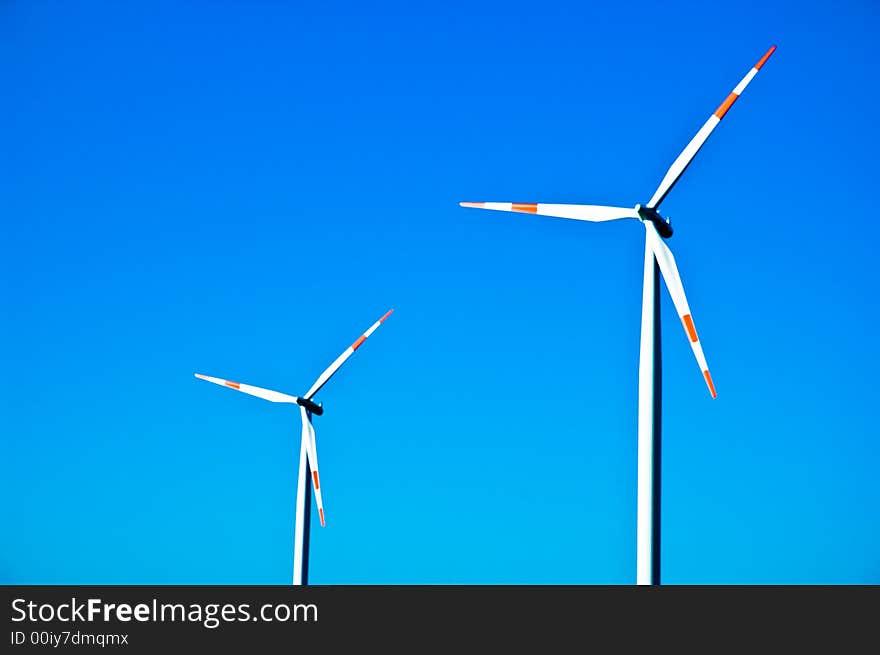 Two electricity generating windmills against a blue sky. Two electricity generating windmills against a blue sky.