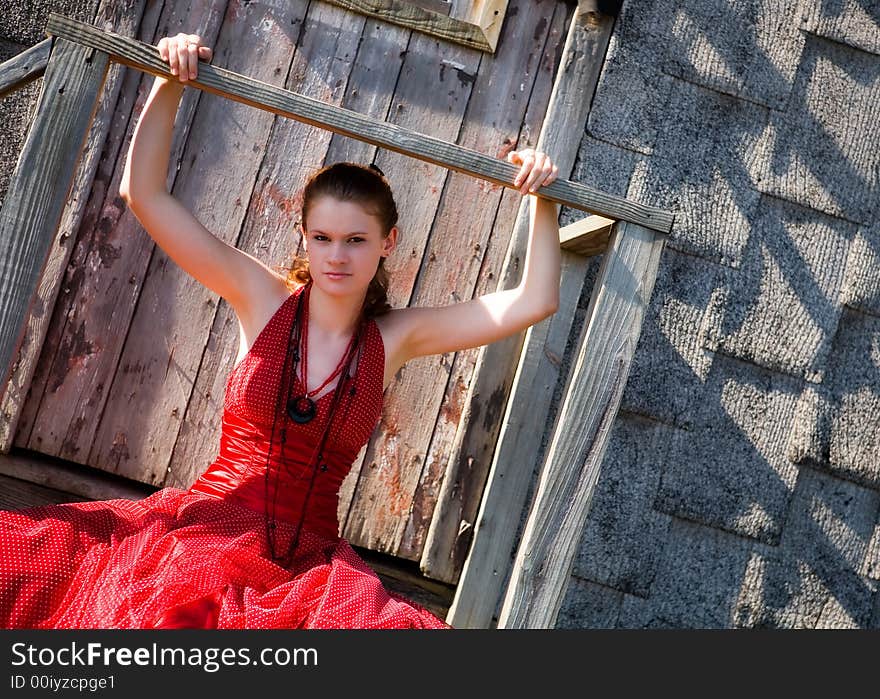 Lovely teen in formal wear sitting on the stoop of a tumble-down shack while hanging onto its broken railing. Lovely teen in formal wear sitting on the stoop of a tumble-down shack while hanging onto its broken railing.