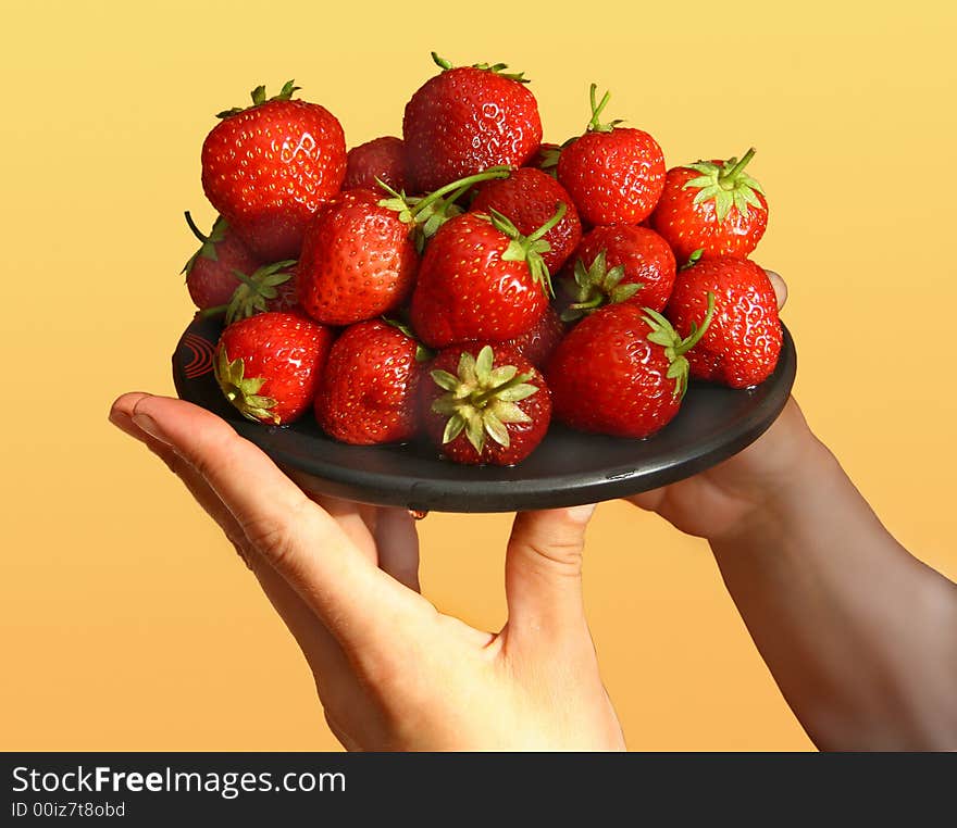 Black plate with a strawberry in female hands. Black plate with a strawberry in female hands.