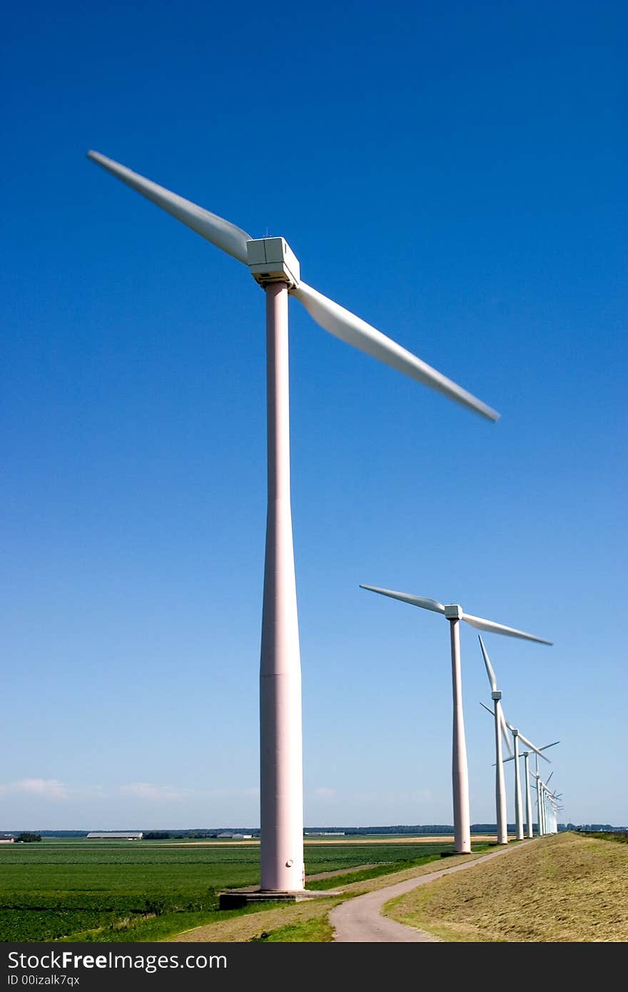 Wind turbines lined up along a road, against a clear blue sky. Wind turbines lined up along a road, against a clear blue sky